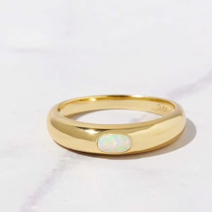 May include: A gold ring with a white opal gemstone set in the center. The ring has a rounded band.