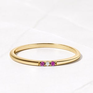 May include: A delicate gold band ring with three small gemstones: two pink sapphires and a white diamond.