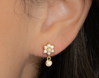 Puede incluir: Pendientes de oro en forma de flor con una sola perla que cuelga del centro. Los pendientes se llevan en la oreja de una persona.