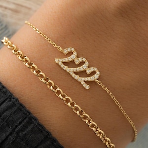 May include: A gold chain bracelet featuring a delicate chain and a charm that reads "2023" in sparkling diamonds.