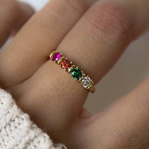 May include: A gold ring with five colourful gemstones. The ring features a pink, orange, green, and clear stone.