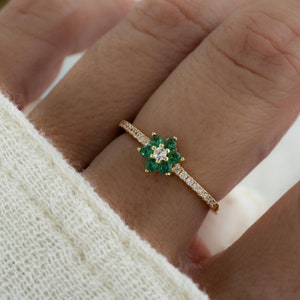 May include: A gold ring with a green flower design. The flower has a single white stone in the center and is surrounded by smaller green stones.