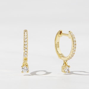 May include: A pair of gold hoop earrings with a small dangling crystal. The hoops are set with small clear crystals.