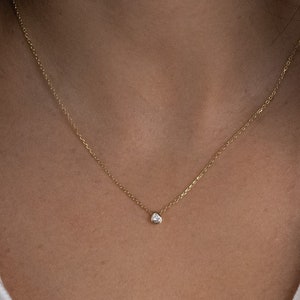 May include: A delicate gold chain necklace with a small, clear gemstone pendant.