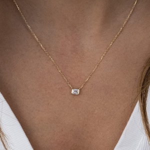May include: A delicate gold chain necklace with a small, rectangular, clear gemstone pendant.