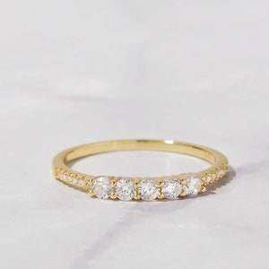May include: A gold band ring with a row of small clear stones set in the band.