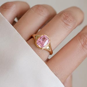 Elongated pink cubic zirconia ring in gold, worn on the hand as a cushion cut statement ring