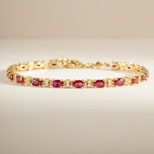 Könnte beinhalten: Ein goldenes Armband mit einer Reihe oval geschliffener, tief pink-roter Edelsteine, die sich mit kleinen, klaren, rund geschliffenen Steinen abwechseln. Die Metallglieder verbinden jede Steinfassung in einer durchgehenden Linie mit Verschluss.