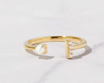 Puede incluir: Un anillo de oro con una piedra de ópalo blanco en un lado y una fila de pequeñas piedras transparentes en el otro.