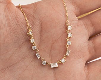 May include: A delicate gold necklace with a series of clear, sparkling gemstones. The necklace features a mix of round and baguette-cut stones, set along a fine gold chain. The gemstones are evenly spaced, creating a subtle, elegant design.