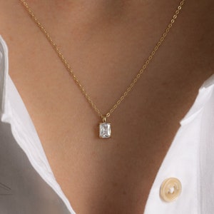 May include: A delicate gold chain necklace with a small square-shaped clear gemstone pendant.