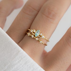 以下が含まれることがあります： 薄い青色の宝石と透明なキュービックジルコニアの石がついた、ゴールドのリング3つのセット。リングは繊細で上品で、重ね付けに最適です。