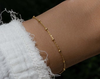 May include: A delicate gold chain bracelet with small round beads.