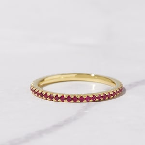 May include: A thin gold band ring with a row of small red ruby stones.