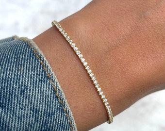 Puede incluir: Un brazalete de tenis de oro con pequeños diamantes transparentes engastados en pavé.