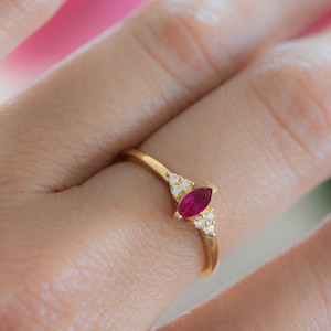 Könnte beinhalten: Ein goldener Ring mit einem rubinroten Marquise-Schliff und kleinen Diamanten.