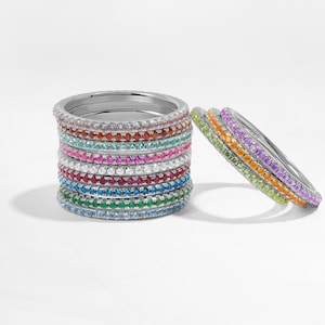 May include: A stack of colorful, thin, silver rings with small gemstones. The rings are arranged in a rainbow pattern, with each ring featuring a different color of gemstone.