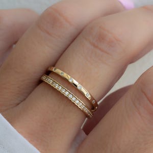 Puede incluir: Dos anillos de oro con pequeños diamantes. El anillo superior tiene una fila de diamantes y el anillo inferior tiene diamantes dispersos.