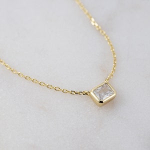 Puede incluir: Un delicado collar de cadena de oro con un pequeño colgante de piedra preciosa rectangular transparente.
