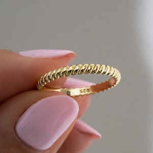 May include: A gold-toned ring with a twisted rope design. The ring is marked with the number "925" on the inside.