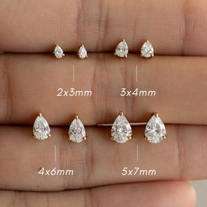 May include: A selection of gold stud earrings featuring pear-shaped, clear gemstones. Sizes are labelled as 2x3mm, 3x4mm, 4x6mm, and 5x7mm. The earrings are presented against a light backdrop.