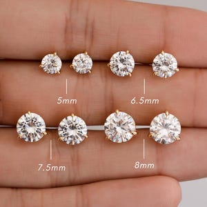 May include: A selection of gold-colored stud earrings with clear, round cubic zirconia stones. Sizes range from 5mm to 8mm. The earrings are displayed on a light-colored background.
