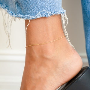 May include: A gold chain anklet on a person's ankle. The anklet is thin and delicate.