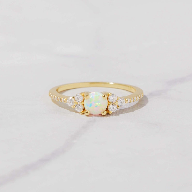May include: A gold ring with a white opal gemstone surrounded by smaller clear gemstones