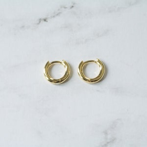 May include: A pair of gold hoop earrings. The hoops are thick and have a slightly rounded shape.