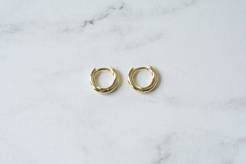 May include: A pair of gold hoop earrings. The hoops are thick and have a slightly rounded shape.