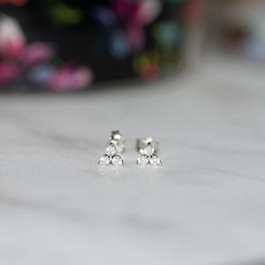 May include: A pair of silver stud earrings with three small, clear cubic zirconia stones arranged in a triangular shape.