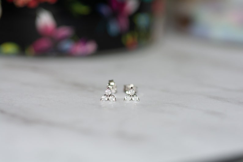 May include: A pair of silver stud earrings with three small, clear cubic zirconia stones arranged in a triangular shape.