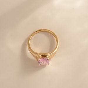 Top-down view of an elongated cushion cut ring statement gold with a pink stone.