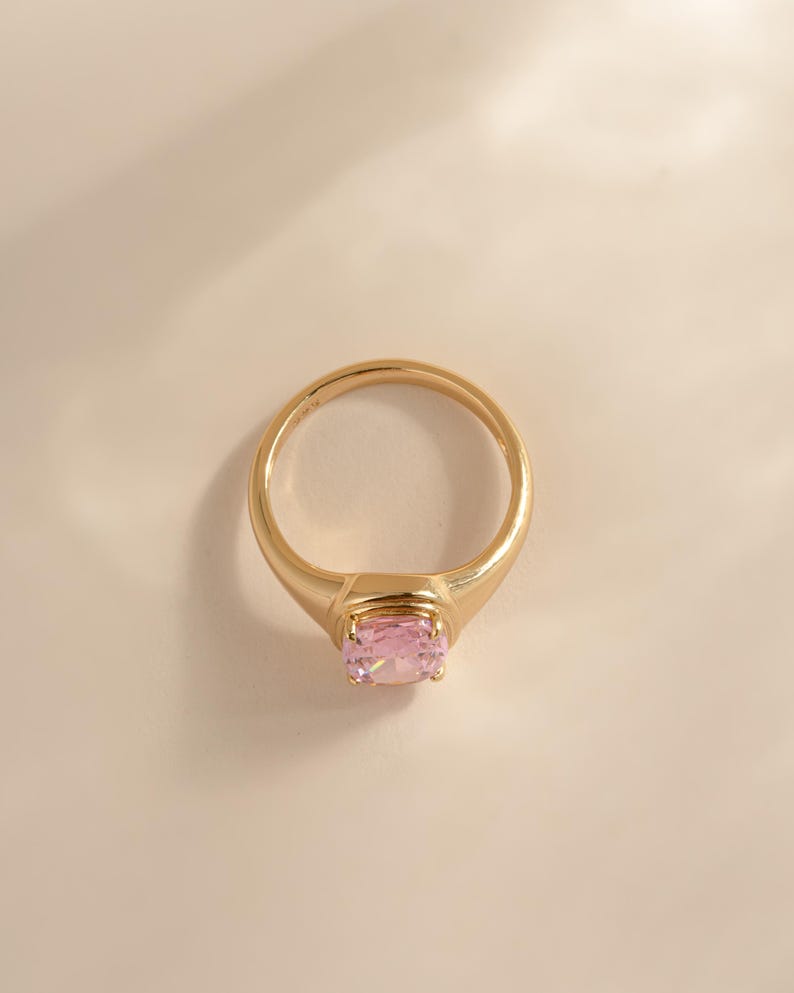 Top-down view of an elongated cushion cut ring statement gold with a pink stone.