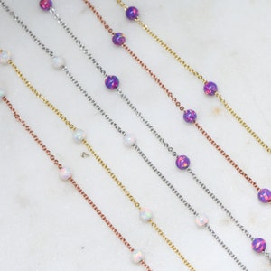 May include: Five delicate necklaces with alternating opal and iridescent purple beads. The necklaces are layered on a white surface.