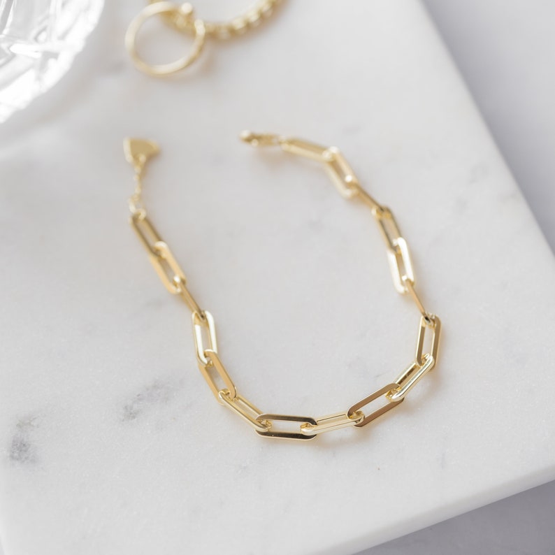May include: A gold chain bracelet with a simple, linked design. The bracelet is made of a series of connected oval-shaped links.