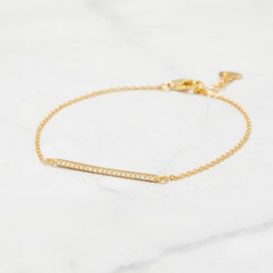 May include: A delicate gold chain bracelet with a thin bar charm set with small white stones.