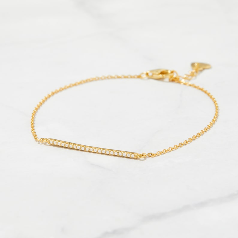 May include: A delicate gold chain bracelet with a thin bar charm set with small white stones.