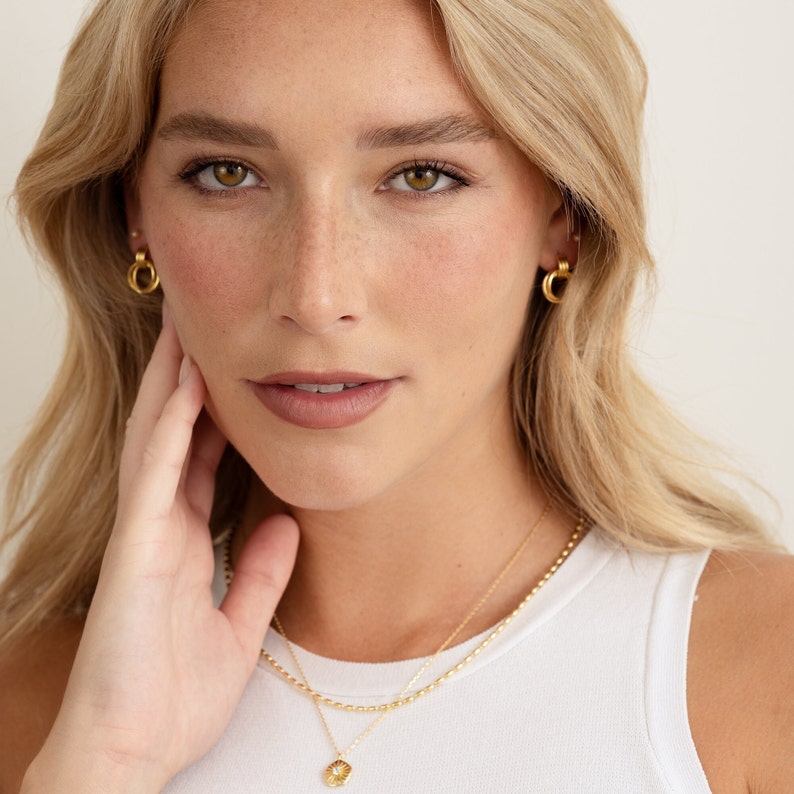 model wearing gold knot hoops with small studs, paired with a gold rice bead necklace and starburst medallion
