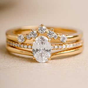 Gold bridal jewelry featuring a gold stacking ring set  with an oval cut ring on a beige minimalist background