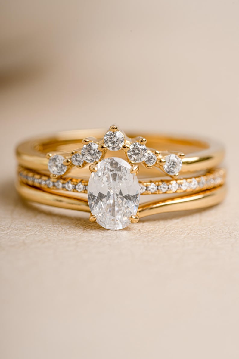 Gold bridal jewelry featuring a gold stacking ring set  with an oval cut ring on a beige minimalist background