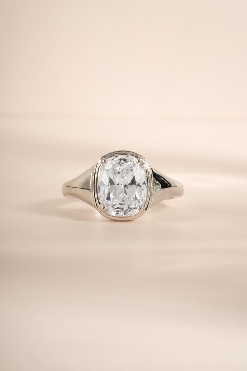 Elongated diamond ring in sterling silver with a bezel-set cushion cut stone.