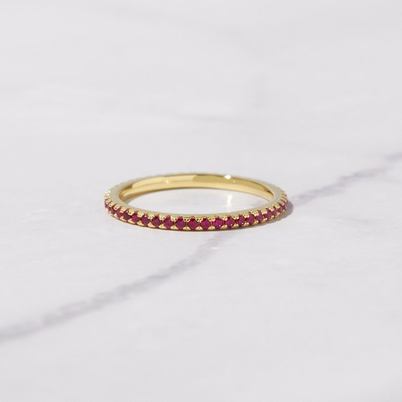 Puede incluir: Un fino anillo de banda de oro con una fila de peque&ntilde;as piedras preciosas rojas.
