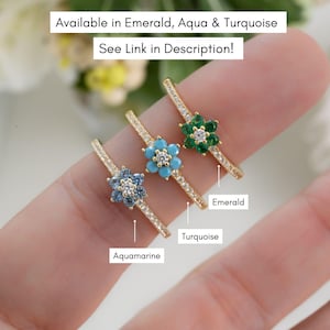 May include: Three gold rings with flower-shaped settings. The rings are set with different colored gemstones: aquamarine, turquoise, and emerald. The rings are labeled with the gemstone names.