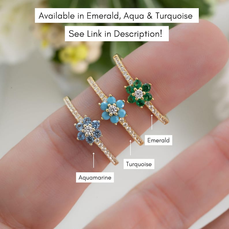May include: Three gold rings with flower-shaped settings. The rings are set with different colored gemstones: aquamarine, turquoise, and emerald. The rings are labeled with the gemstone names.