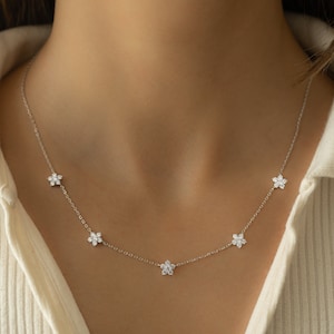 Pu&ograve; includere: Una delicata collana a catena d'argento con cinque piccoli ciondoli a forma di fiore, ognuno adornato con scintillanti pietre di zircone cubico trasparenti.