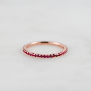 Puede incluir: Un delicado anillo de banda de oro rosa con una fila de peque&ntilde;as piedras de rub&iacute; rojo brillante.