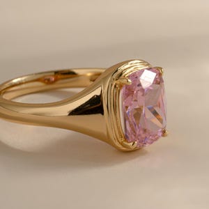 Side view of an elongated cushion cut solitaire ring in gold with a pink cubic zirconia stone.