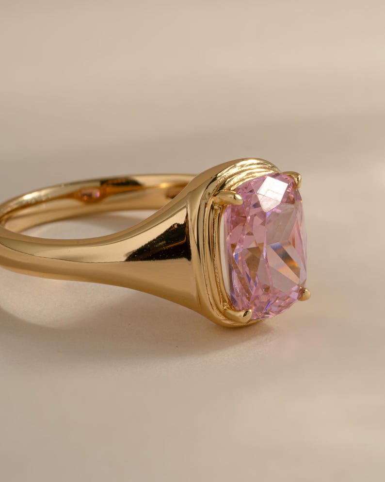 Side view of an elongated cushion cut solitaire ring in gold with a pink cubic zirconia stone.