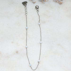 May include: A silver chain bracelet with five white opal beads. The bracelet has a heart-shaped clasp.